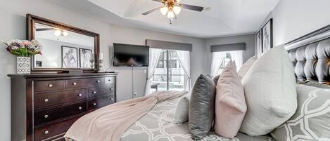 A bedroom with a bed, dresser, television, and a ceiling fan.