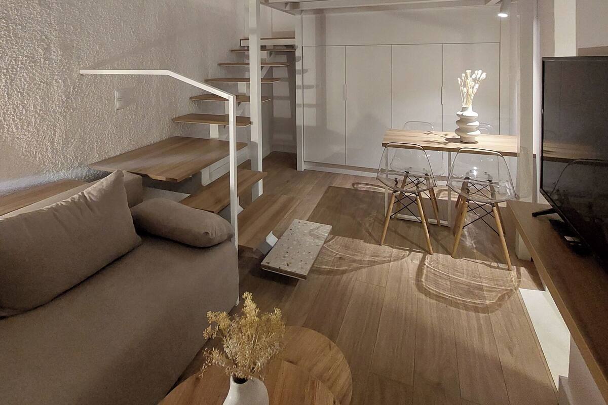 Een moderne woonkamer met een stapelbed, een bank, een eettafel met stoelen en een trap.