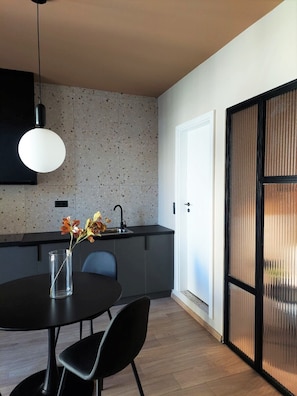 A modern kitchen with a round dining table, black chairs, a hanging light fixture, and a backsplash with speckled tiles.