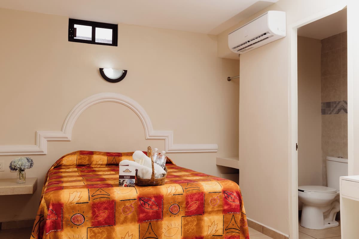 Une chambre d’hôtel avec un lit, une table de chevet, un vase de fleurs et un appareil de climatisation.
