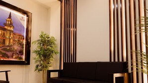 Un interior moderno con un sofá oscuro, un cuadro enmarcado de un edificio, listones verticales de madera y dos plantas en macetas.
