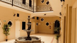 Un amplio atrio con una fuente central, varias puertas y apliques decorativos.