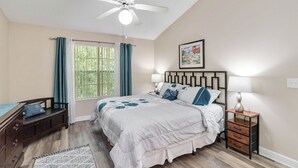 A bedroom with a bed, bedside tables, a ceiling fan, and a window with curtains.
