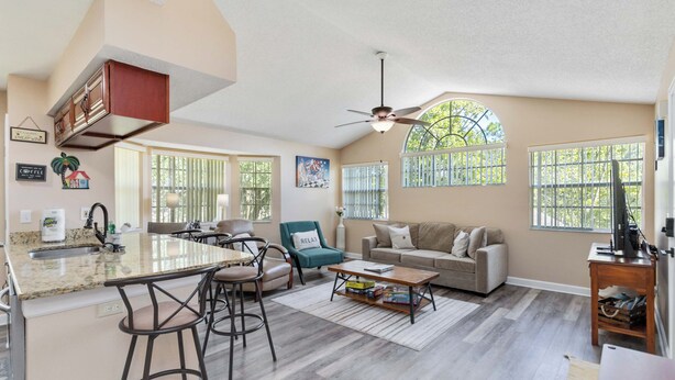 A spacious living area with a kitchen island, bar stools, a sofa, and a coffee table.