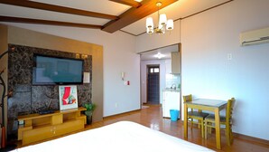 A hotel room with a bed, a TV mounted on a stone wall, a wooden ceiling, and a dining area with a table and chairs. - New Beachscape (Jeju City)