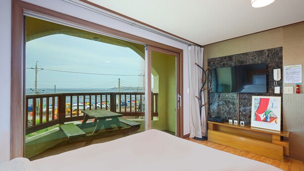 A hotel room with a balcony, a bed, a TV, and a painting on the wall. - New Beachscape (Jeju City)