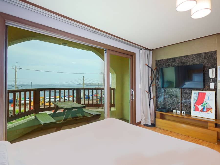 A hotel room with a balcony, a bed, a TV, and a painting on the wall.