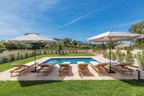 A pool area with six wooden lounge chairs and two umbrellas, surrounded by a well-maintained lawn and a view of distant hills. - Villa JP Avec Piscine à 5 min de la Plage de Calvi (Calvi)