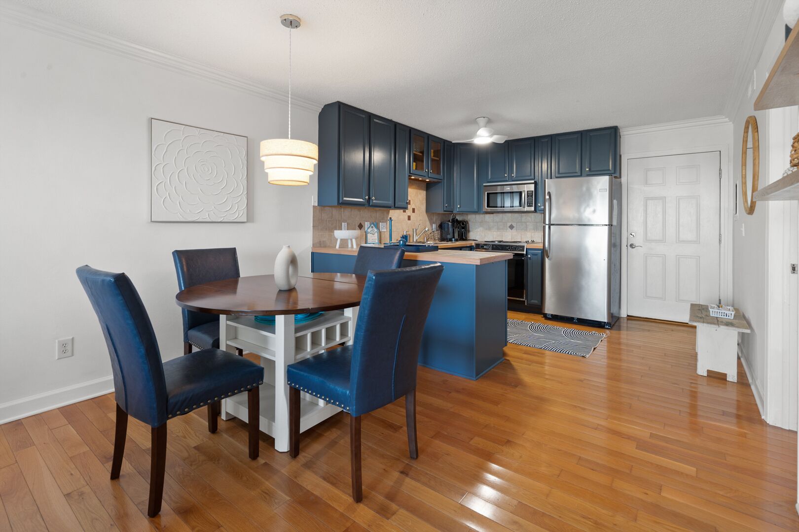 Een moderne keuken met donkerblauwe kastjes, een roestvrijstalen koelkast en een eethoek met blauwe stoelen en een houten tafel.
