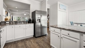 A modern kitchen with white cabinetry, a stainless steel refrigerator, granite countertops, and a wooden floor. - Rare find in the heart of North Myrtle Beach (North Myrtle Beach)