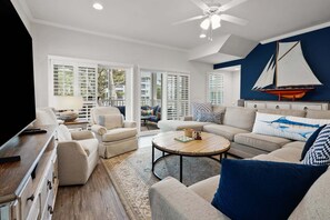 A living room with a TV, sofa, armchairs, a coffee table, and a sailboat decoration on the wall.