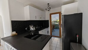 A modern kitchen with white cabinets, a black countertop, and a built-in oven. There is a wooden door leading to a balcony with outdoor furniture. - Villa Familiale Superbe vue mer et Couchers de Soleil (Pietrosella)