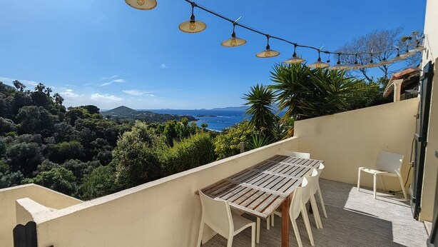 A balcony with a wooden table and chairs, overlooking a coastal landscape with trees and a view of the sea. - Villa Familiale Superbe vue mer et Couchers de Soleil (Pietrosella)