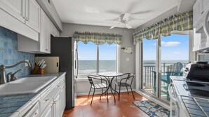 A kitchen with a large window overlooking the ocean, a dining area with chairs, and a ceiling fan. - Indulge in stunning views from this expansive oceanfront condo featuring a large balcony and pool (North Myrtle Beach)