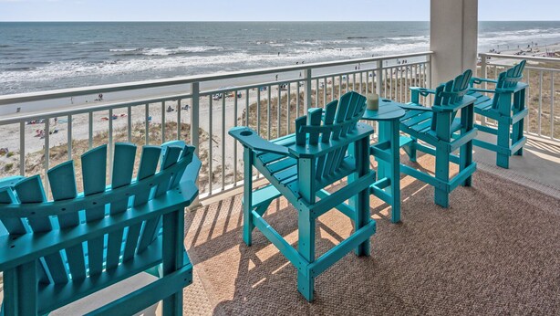 A covered outdoor seating area with chairs and tables overlooking a beach. - Indulge in stunning views from this expansive oceanfront condo featuring a large balcony and pool (North Myrtle Beach)
