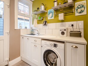 A compact kitchen with a washing machine, a toaster, and a sink. - Beachcombers Retreat (Felixstowe)