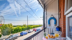 A balcony with a table set for breakfast, overlooking a street with parked cars and a body of water in the background.