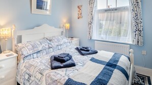 A bedroom with a bed, nightstands, a window with curtains, a framed picture on the wall, and a wall-mounted decoration.