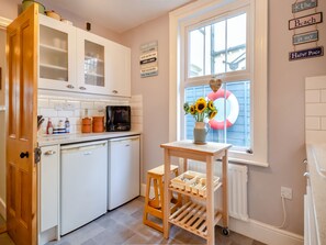 A kitchen with white cabinets, a coffee maker, and a vase with sunflowers by a window with a pink and white decoration.