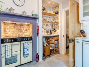 A kitchen with a brick wall, a stove, and shelves with kitchenware. - Beachcombers Retreat (Felixstowe)