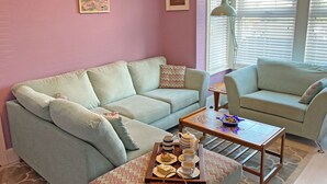 Uma sala de estar com um sofá azul claro, uma poltrona combinando e uma mesa de centro com uma bandeja de doces e xícaras.