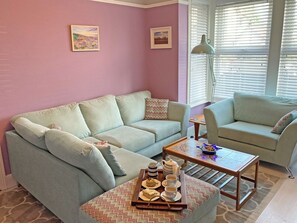 A living room with a light blue sofa, a matching armchair, and a coffee table with a tray of pastries and cups. - Beachcombers Retreat (Felixstowe)