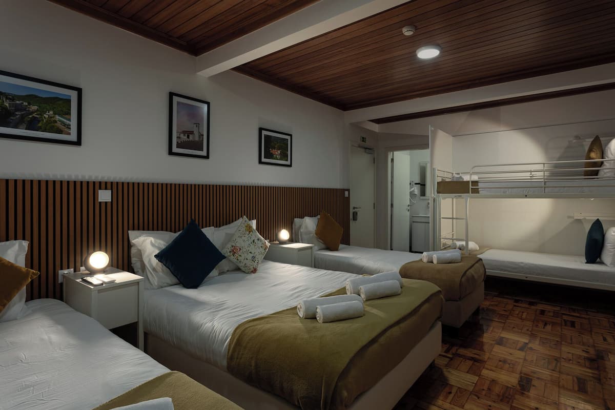 A hotel room with two beds, a bunk bed, wooden paneling on the walls, and framed pictures on the wall.