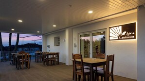 An indoor dining area with wooden tables and chairs, a glass door leading outside, and a sign reading "Logia do Cantoneiro". - Guest House A Loja do Cantoneiro (Albergaria-a-Velha)