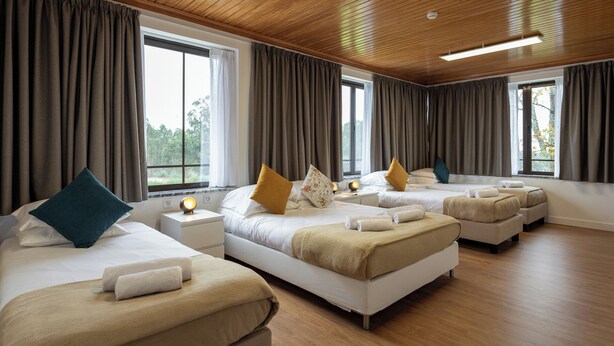 A hotel room with three beds, wooden ceiling, large windows, and a view of greenery. - Guest House A Loja do Cantoneiro (Albergaria-a-Velha)