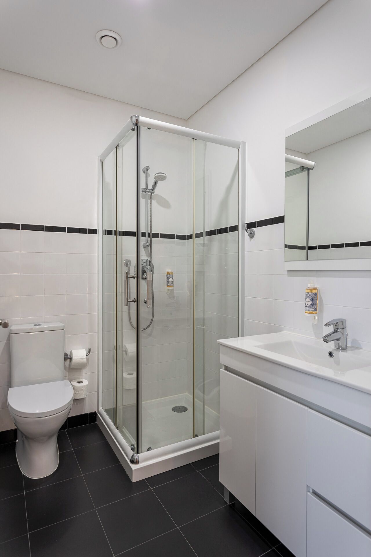A modern bathroom with a glass-enclosed shower, a toilet, and a sink with a mirror above.