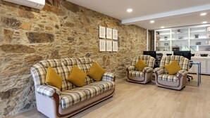 A cozy room with a stone wall, two plaid sofas with yellow cushions, and a wooden floor. - Guest House A Loja do Cantoneiro (Albergaria-a-Velha)