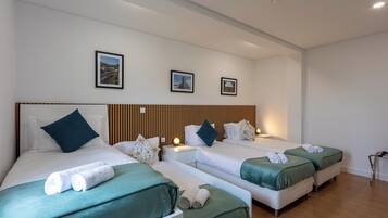 Een hotelkamer met drie eenpersoonsbedden, elk met een groene sprei en witte kussens. Boven de bedden hangen afbeeldingen in lijsten.