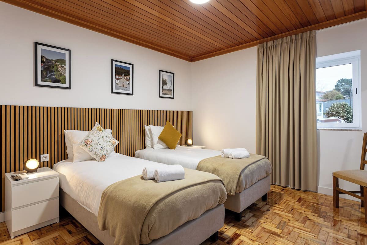 A hotel room with two beds, a wooden ceiling, and a window with curtains.