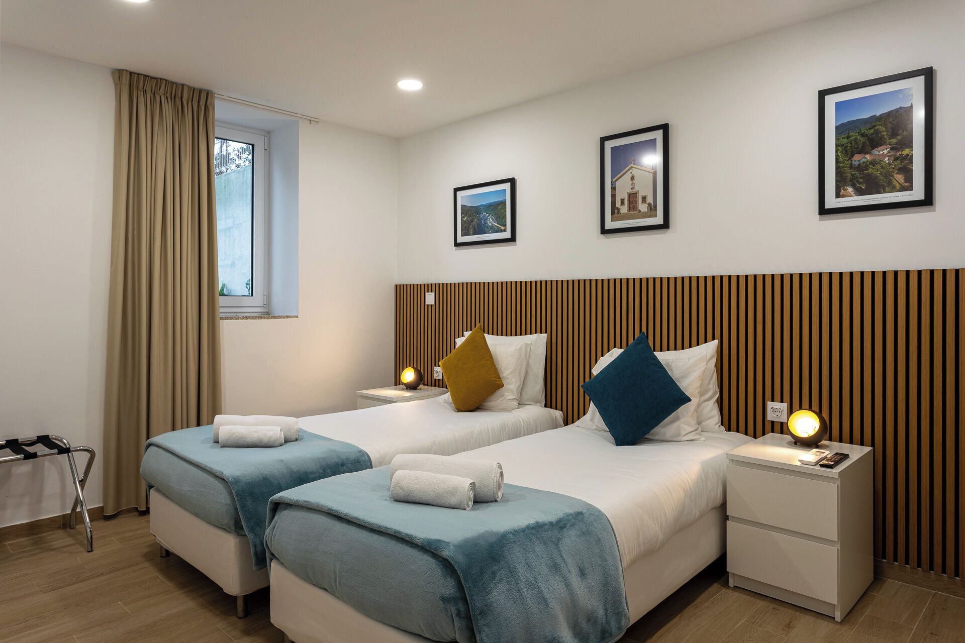 Ein Hotelzimmer mit zwei Betten, einem Fenster mit Vorhängen und gerahmten Bildern an der Wand.