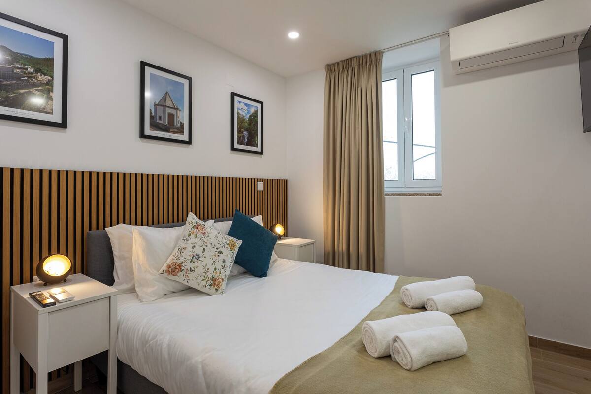 A neatly arranged hotel room with a bed, two bedside tables, a nightstand, a window with curtains, and two framed pictures on the wall.