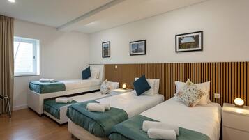 Habitación de hotel con tres camas, cada una con ropa de cama verde y almohadas blancas. Se observan cuadros enmarcados en la pared, una ventana con cortinas y un cabecero de madera.