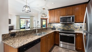 A modern kitchen with granite countertops, stainless steel appliances, wooden cabinets, and a stone backsplash. - 2Bed/2Bath Mountain Getaway with Pool/Hot Tub (Canmore)