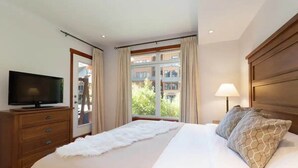 A bedroom with a bed, a television on a wooden dresser, a window with curtains, and a lamp on the nightstand. - 2Bed/2Bath Mountain Getaway with Pool/Hot Tub (Canmore)