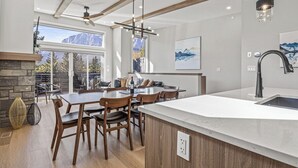 A modern kitchen with a large island, wooden chairs, and a stone fireplace.