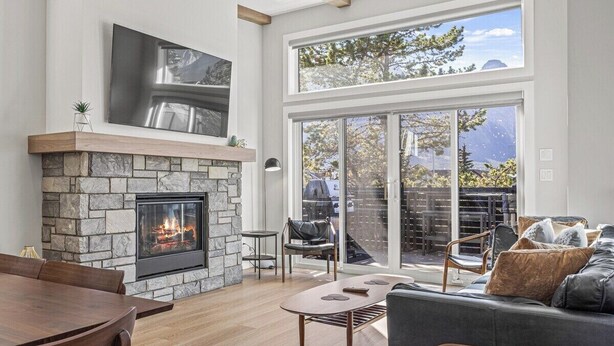 A modern living room with a stone fireplace, a flat-screen TV, and a large sliding glass door leading to an outdoor patio.