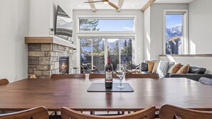 A spacious dining area with a large wooden table and chairs, a fireplace, and a view of mountains through large windows.