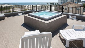 Eine Dachterrasse mit Whirlpool, weißen Kunststoffstühlen und Blick auf Strand und Meer.