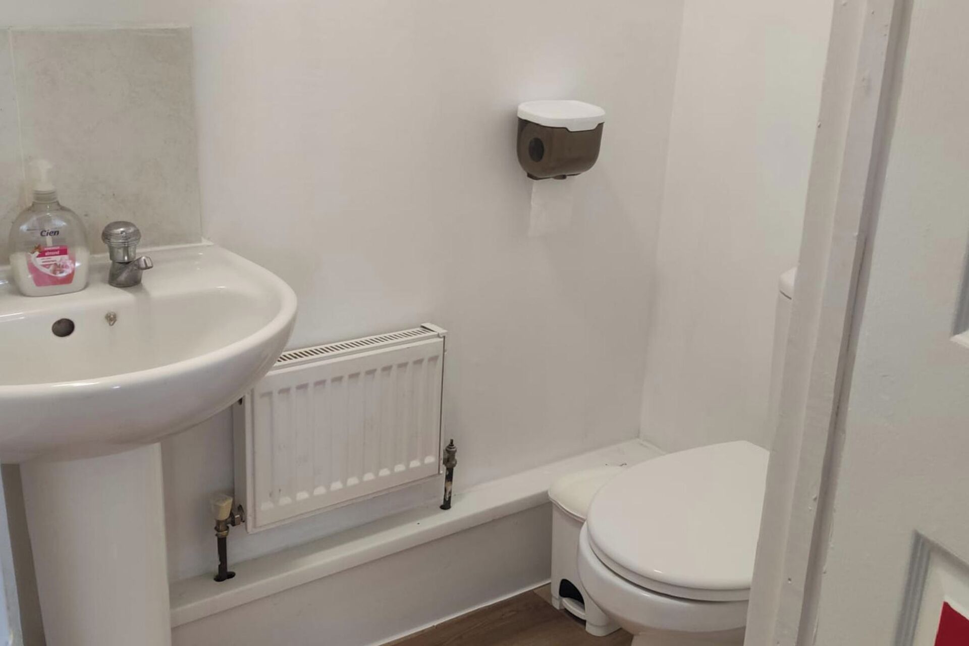 A small, clean bathroom with a white sink, toilet, and radiator.