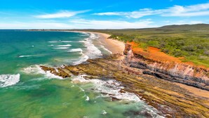 A coastal landscape with a rocky shoreline, a beach, and a distant view of a town. - Aqua Vista - Beach Front Location (Brooms Head)