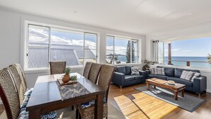 A spacious living room with a large table, two sofas, and a view of the ocean. - Aqua Vista - Beach Front Location (Brooms Head)