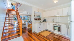A modern kitchen with white cabinets, a built-in oven, and a wooden staircase leading to a balcony with a view of the sea. - Casa della vista - Beach Front Location (Brooms Head)