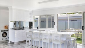 A modern kitchen with white cabinetry, a built-in washing machine, and a large island with bar stools. - A Little Beach Haven - In the heart of Brooms Head (Brooms Head)