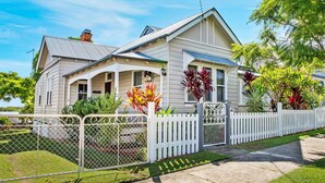 Een twee verdiepingen tellend huis met een witte picket fence, een overdekte veranda en een verzorgd gazon.