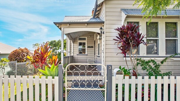 Een huis met een overdekte veranda, een witte picket fence en diverse planten.