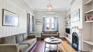 Een woonkamer met een bank, fauteuil, ronde tafel, open haard en decoratieve objecten.